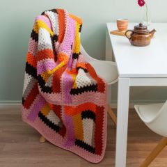Molla Mills Kaiku Blanket on a chair. The blanked is crocheted with Lankava Lysti Yarn using colors Desert rose 872, Cotton candy 871, Saffron 866, Snow 851, Coffee 868, Marigold 878, Dandelion 864 and Greige 870.