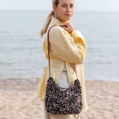 Hertta-laukku näyttelijä Iina Kuustosen olalla rannalla. Laukku virkataan Lankava Essi -ontelokuteesta väreillä musta 20 ja pellavanbeige 24.