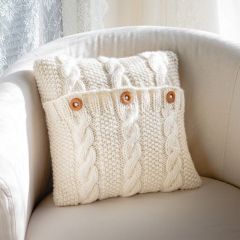 Lempi-palmikkotyyny nojatuolilla. Tyyny neulotaan Lankava Lempi -villalangasta värillä luonnonvalkoinen 101.