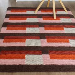 Molla Mills Kulma Rug on the floor. The rug is crocheted with Lankava Frotee Loopy Craft Yarn using colors cocoa 55, chalk pink 89 and burnt orange 58 as well as with Lankava Lilli Tube Yarn using colors natural white 2 and terracotta 36.
