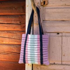 Raita-makrameekassi ripustettuna. Kassi solmeillaan Lankava Minimop -langasta väreillä laventeli 85, laivastonsininen 74, vaaleanpunainen 81, valkoinen 51 ja jäänsininen 88.