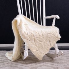 Talviuni-torkkupeitto keinutuolin päällä. Peitto neulotaan Esito-lenkkimohairista sävyssä valkaistu 0001 sekä Lankava Into -villalangasta sävyssä luonnonvalkoinen 1012.