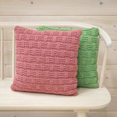 Free pattern: Two textured Päre Cushion Covers on a couch. The cushion cover on the front is knitted with Lankava Essi Tube Yarn using colour dark rose 13 and the one on the back using colour green 10.