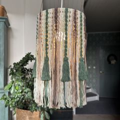 Sävy-makramé lampskärm hänger från taket. Lampskärmen knyts av Lankavas Minimop-garn i färgerna mörkgrön (61), ljusgrön (84), greige (87), linnebeige (73) och kakao (55).